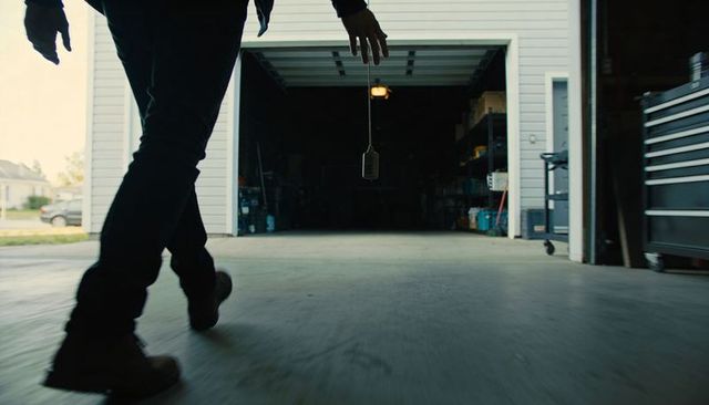 Walking figure approaching open garage door with dangling key fob, suburban driveway