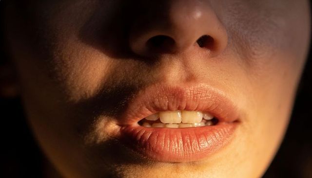Closeup female lower face with slightly parted lips and visible teeth in dramatic light