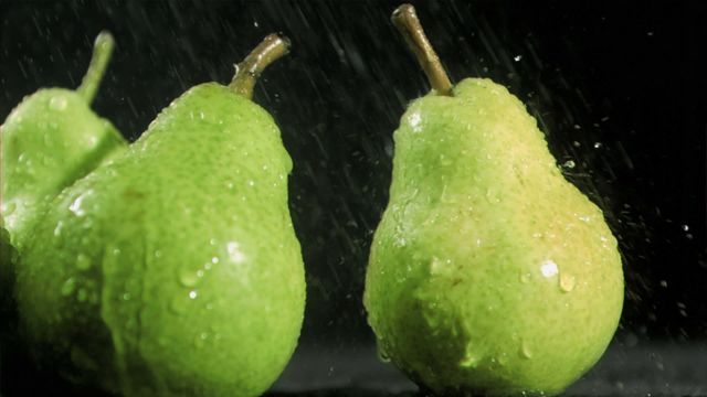 Ripe green pears displaying water droplets, creating a fresh and healthy appearance against a black background. Suitable for use in advertisements promoting fresh produce or healthy eating, as well as in decorating kitchen walls for a vibrant aesthetic. The imagery evokes senses of freshness and vitality, appealing in culinary magazines or health blogs.