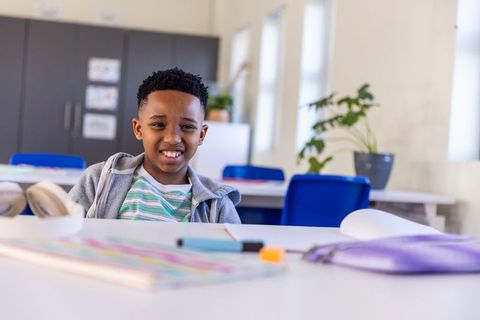 Smiling african american boy sitting at table in bright classroom learning and focusing