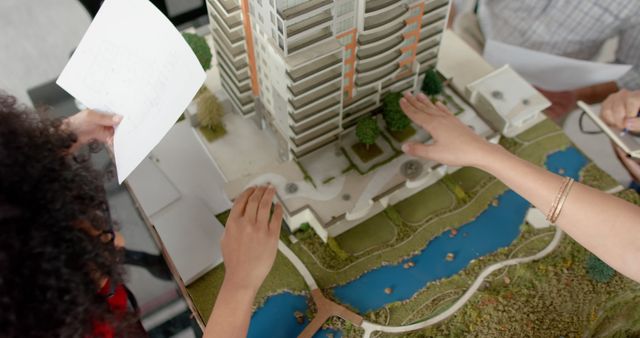 Architects examining a detailed scale model of a modern building along with surrounding landscaping. Perfect for use in articles on architectural design, urban planning, construction projects, real estate development, and team collaboration among architects and designers.