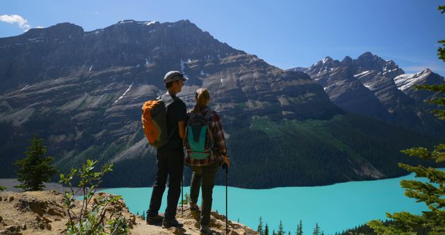 Caucasian tourist couple standing on cliff and looking at mountains by sunny lake. Summer, vacations, traveling and active lifestyle, unaltered.