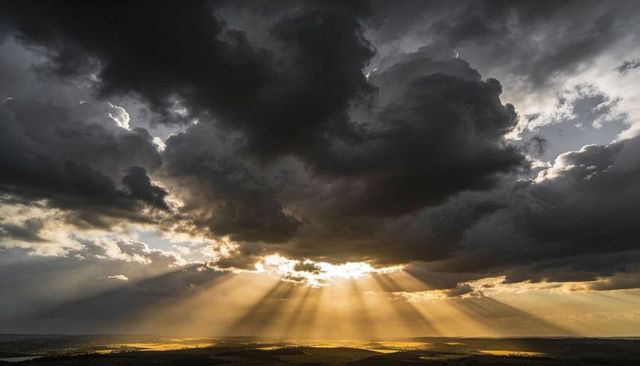Dramatic Sunbeams Piercing Storm Clouds Over Patchwork Farmland at Golden Hour