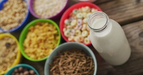 Displaying glass milk bottle with colorful cereal bowls on rustic wood breakfast table
