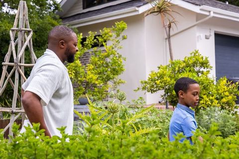 African american father walking with son along lush front yard garden path near trellis