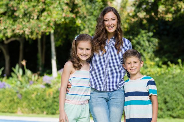 Mother standing with her son and daughter in a lush garden, all smiling and enjoying a sunny day. Ideal for use in family-oriented advertisements, parenting blogs, and lifestyle magazines. Perfect for illustrating concepts of family bonding, outdoor activities, and happy moments.