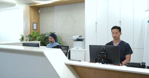 Diverse medical reception staff working at modern clinic front desk with headsets
