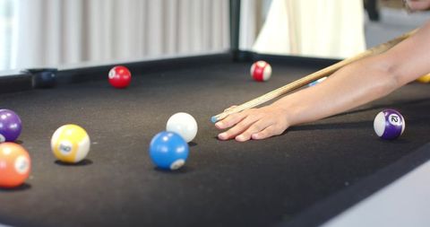 Woman lining up shot on black pool table with cue stick and colorful billiard balls
