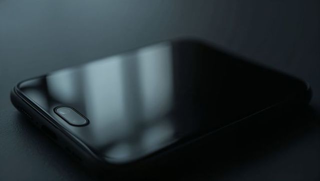 Resting black smartphone showing window reflection and oval fingerprint sensor