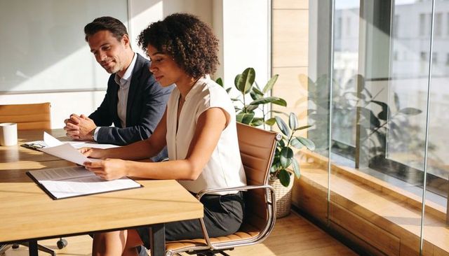 Businesswoman reviewing documents with colleague at sunlit office conference table