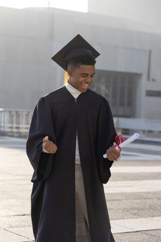African american male graduate celebrating with diploma on urban campus rooftop