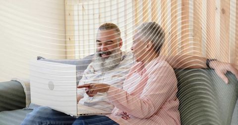 Mature couple sharing laptop on couch, casual conversation and cozy home tech moment