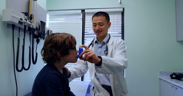 Young asian male doctor helping a caucasian boy patient in using asthma inhaler in clinic. Male doctor holding asthma inhaler. Male doctor interacting with patient 4k