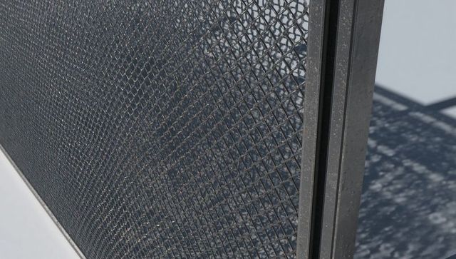 Diamond metal mesh panel throwing geometric shadow on pale gray deck, metal post
