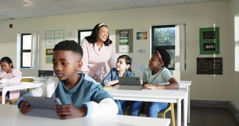 Smiling African American Teacher Guiding Diverse Young Students with Tablets in Classroom