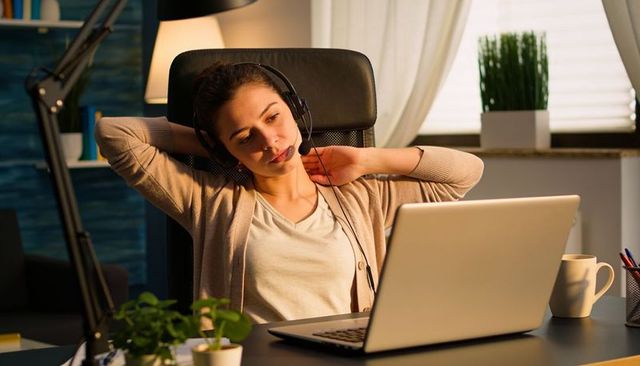 Woman stretching while wearing headset during remote work at home office evening