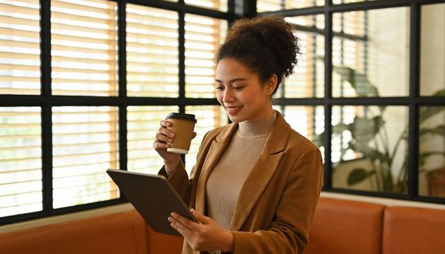 Young professional enjoying coffee while using tablet in modern coworking cafe