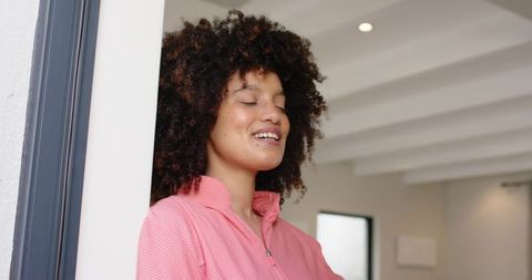 African american woman leaning in doorway smiling with eyes closed wearing pink zip sweatshirt