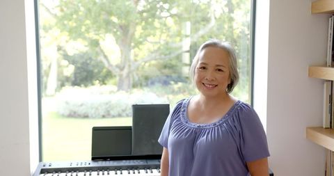 Smiling Senior Woman Standing by Piano in Bright Room
