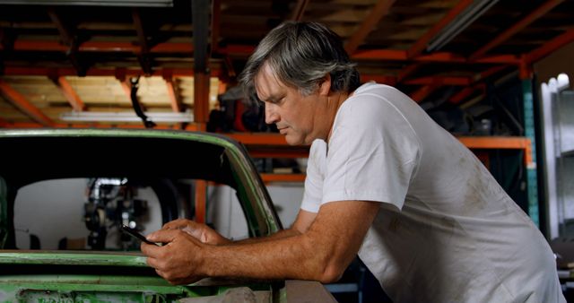 Middle-Aged Mechanic Leaning on Car in Garage using Smartphone - Download Free Stock Images Pikwizard.com