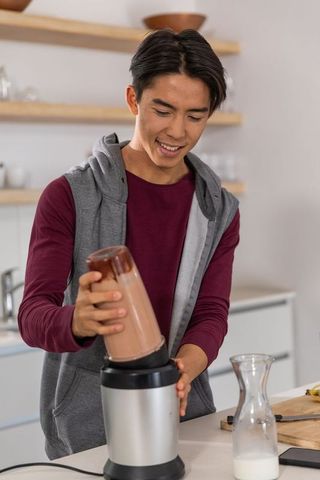 Young asian man making chocolate smoothie with personal blender in modern kitchen