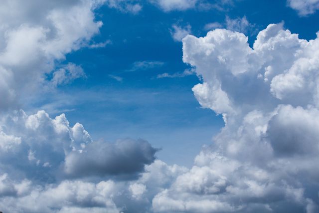 Fluffy white clouds float in a bright blue sky, creating a serene and peaceful atmosphere. Ideal for nature-themed projects, weather-related content, backgrounds for websites and presentations, and mood-enhancing imagery.