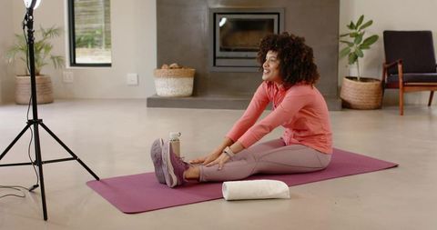 Curly-haired woman stretching on purple yoga mat in modern living room for home workout