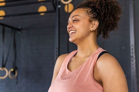 Curly-haired woman smiling during gym workout wearing pink tank top, confident and vibrant