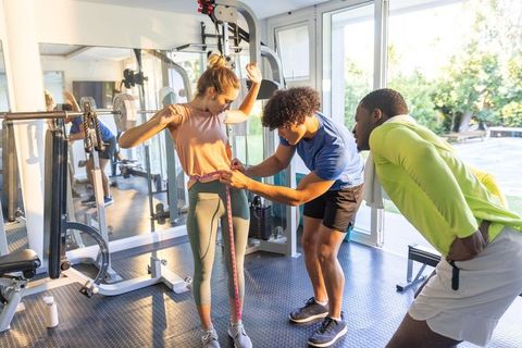 Two trainers measuring female client waist with tape during training session in bright gym