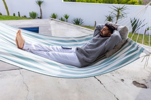 Man relaxing in striped hammock by plunge pool with smartphone on lap