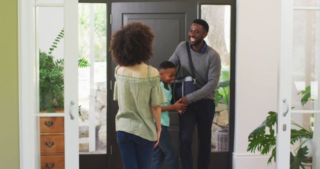 Happy biracial mother and son welcoming father home at front door. Domestic life, family and togetherness.