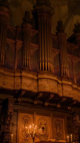 Vertical video showing pipe organ in gothic cathedral with lit candelabrum, antique wood