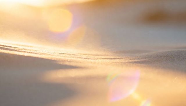 Golden sand ripples glowing at sunset with soft bokeh, warm lens flare and minimal texture