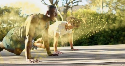 Two men doing push-ups on sunlit wooden deck with golden bokeh flare for fitness