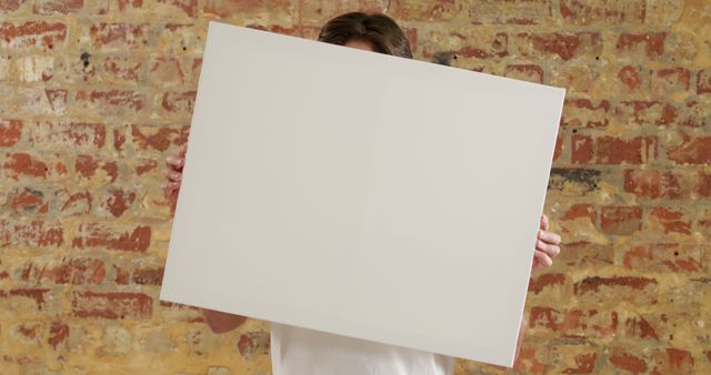Caucasian man holding a blank canvas, with copy space. Ideal for a custom message, the setting suggests a creative studio environment.