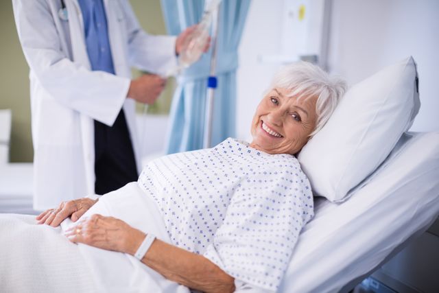Elderly woman lying in a hospital bed, smiling while receiving medical care. A doctor is adjusting an IV drip in the background. This image can be used for healthcare advertisements, medical websites, patient care brochures, and wellness articles.