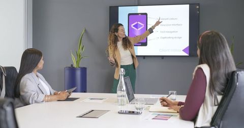 Multicultural women presenting digital design in boardroom during collaborative meeting
