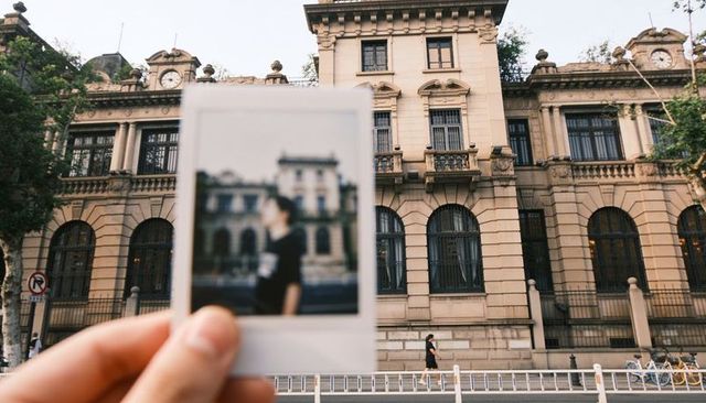 Holding polaroid framing ornate historic facade with blurred portrait on urban street