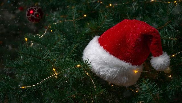 Santa Hat Nestling in Christmas Tree with Warm Fairy Lights and Red Bauble