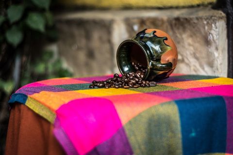 Ceramic mug spilling coffee beans over vibrant plaid cloth on rustic outdoor table