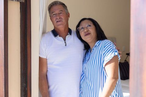 Mixed-ethnicity senior couple embracing and gazing upward in cozy bedroom doorway