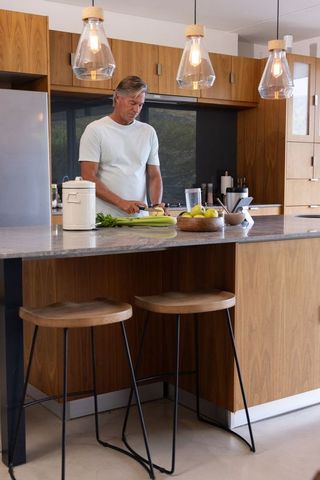 Middle-aged man preparing vegetables at modern wood kitchen island with tablet nearby