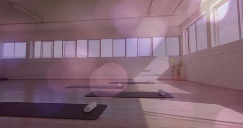 Minimalist yoga studio featuring mats and rolled towels by sunlit windows for calm practice