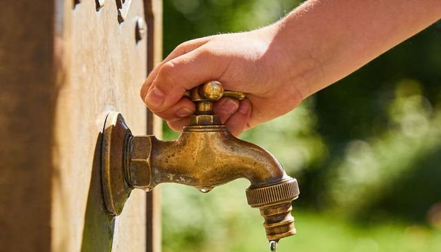 Hand turning brass garden faucet dripping water with weathered patina close-up