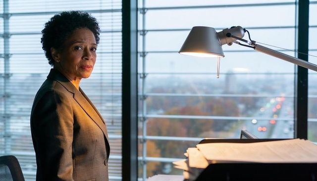 Senior executive standing by office window with cityscape view and documents under lamp