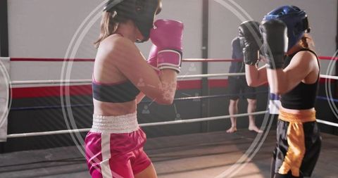 Female boxers sparring in ring wearing headgear and gloves training for competition