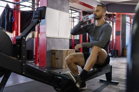 Indian man taking water break on rowing machine in industrial gym during cardio workout
