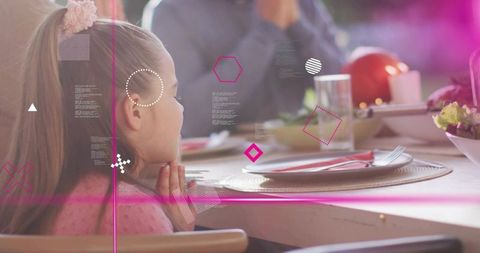 Girl clasping chin at family dinner with pink light overlays, candid mealtime moment