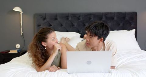 Couple chatting on bed with laptop in modern neutral bedroom, cozy minimalist lifestyle
