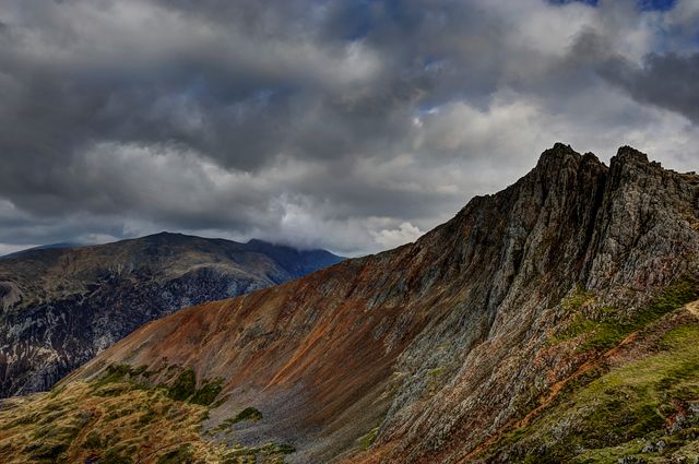 This stunning mountain ridge features a rocky terrain under a sky filled with heavy, dark clouds during the autumn season. The landscape is dramatic, portraying the raw beauty and ruggedness of wilderness. Ideal for usage in travel brochures, nature blogs, outdoor adventure publications, and scenic backgrounds.